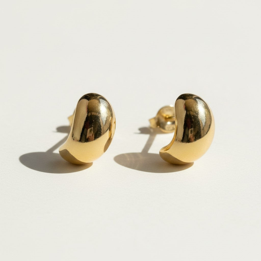 chunky gold dome earrings flat lay, bean shaped gold earrings, sculptural gold stud earrings, high polish gold earrings detail, statement dome earrings, gold earrings push back, modern minimalist gold earrings, glossy gold stud earrings