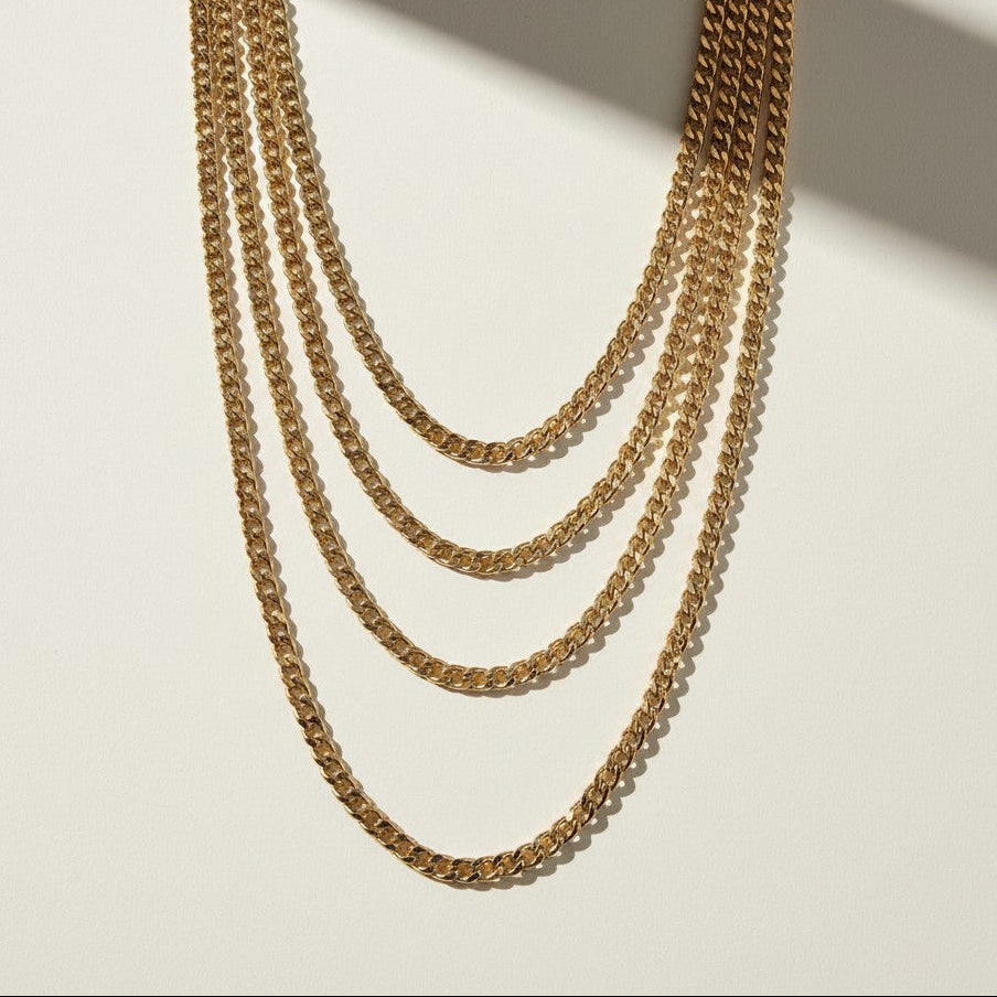 curb chain necklace flat lay, gold curb link necklace detail, classic chain necklace, layered chain necklace, clasp detail necklace, polished chain necklace, gold link necklace, layering necklace set