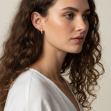 gold baguette hoops on model, huggie hoop earrings worn, emerald huggie hoop earrings, black baguette hoop earrings, clear crystal huggie hoops, gold hoop earrings colorways, baguette stone earrings styled, small gold hoops on ear