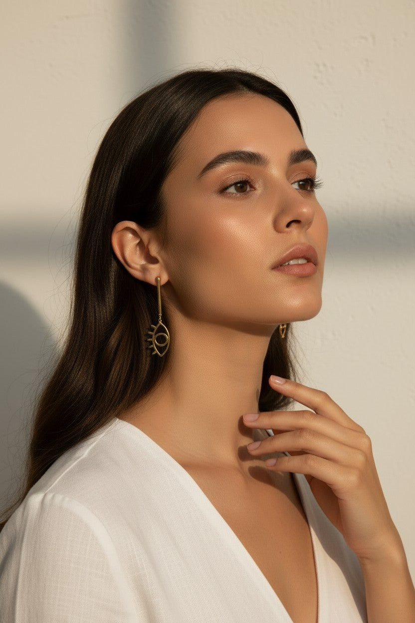 evil eye drop earrings, gold cutout earrings, matte gold dangle earrings, symbolic jewelry, geometric drop earrings, minimalist gold earrings, statement drop earrings, on-model earring photography