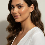 This series of close-up portraits shows the CZ spear charm attached to a small gold seamless hoop, worn at the lobe for a customized, layered earring look. Captured from multiple angles against soft waved hair and a crisp white top, the charm's graduated cubic zirconia setting and tapered point are shown at true scale, giving shoppers a clear sense of drop length and how the 18k gold overlay charm pairs with the 9mm or 11mm hoop.
