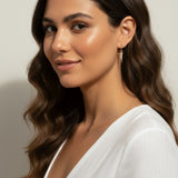 This series of close-up portraits shows the CZ spear charm attached to a small gold seamless hoop, worn at the lobe for a customized, layered earring look. Captured from multiple angles against soft waved hair and a crisp white top, the charm's graduated cubic zirconia setting and tapered point are shown at true scale, giving shoppers a clear sense of drop length and how the 18k gold overlay charm pairs with the 9mm or 11mm hoop.