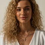 Gold Pavé Cross Pendant Necklace Worn On-Model, This series of portraits shows the gold pavé cross pendant resting at the collarbone on a fine ball chain, styled with a flowing white wrap top for a soft, natural look. Captured from front-facing and close-up profile angles, the crystal-covered cross is shown at true scale against warm skin, giving shoppers a clear sense of its petite, delicate proportions and dainty drop length.