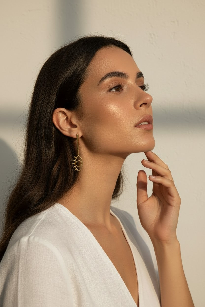 evil eye drop earrings, gold cutout earrings, matte gold dangle earrings, symbolic jewelry, geometric drop earrings, minimalist gold earrings, statement drop earrings, on-model earring photography