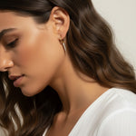This series of close-up portraits shows the CZ spear charm attached to a small gold seamless hoop, worn at the lobe for a customized, layered earring look. Captured from multiple angles against soft waved hair and a crisp white top, the charm's graduated cubic zirconia setting and tapered point are shown at true scale, giving shoppers a clear sense of drop length and how the 18k gold overlay charm pairs with the 9mm or 11mm hoop.