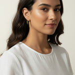 Gold Spike Charm Hoop Earrings Worn On-Model, dangling triangular spike charm at the bottom, worn together with a thin ear cuff along the upper ear for a curated, layered ear stack look. Captured from front-facing, side-profile, and close-up angles, the earrings are shown at true scale against soft waved hair and a crisp white top, giving shoppers a clear sense of the charm's drop length and how the pieces sit together