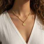 This series of close-up portraits shows a gold curb chain necklace featuring a round coin pendant engraved with a classical winged figure, worn at the collarbone for a layered, vintage-inspired look. Captured on two different models from front-facing and side-profile angles, the pendant's textured beaded border and detailed relief engraving are shown at true scale, giving shoppers a clear sense of the coin's dimension and how the substantial curb chain sits against the neckline