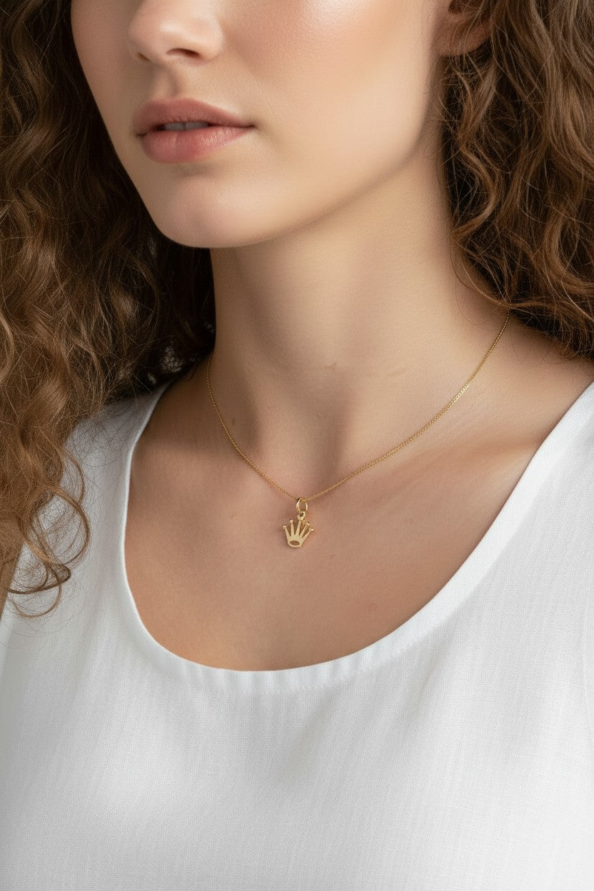 gold crown pendant resting at the collarbone on a fine box chain, styled with a simple white scoop-neck top for a clean, elevated look. Captured from front-facing and close-up angles, the open crown silhouette and its cubic zirconia-tipped points are shown at true scale against soft, warm-toned skin, giving shoppers a clear sense of the pendant's petite, delicate proportions and dainty drop length Crown Pendant Necklace Worn On-Model
