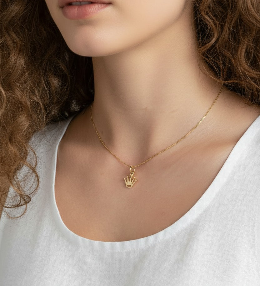 gold crown pendant resting at the collarbone on a fine box chain, styled with a simple white scoop-neck top for a clean, elevated look. Captured from front-facing and close-up angles, the open crown silhouette and its cubic zirconia-tipped points are shown at true scale against soft, warm-toned skin, giving shoppers a clear sense of the pendant's petite, delicate proportions and dainty drop length Crown Pendant Necklace Worn On-Model