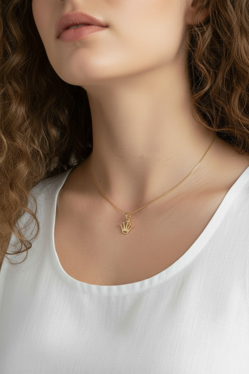 gold crown pendant resting at the collarbone on a fine box chain, styled with a simple white scoop-neck top for a clean, elevated look. Captured from front-facing and close-up angles, the open crown silhouette and its cubic zirconia-tipped points are shown at true scale against soft, warm-toned skin, giving shoppers a clear sense of the pendant's petite, delicate proportions and dainty drop length Crown Pendant Necklace Worn On-Model