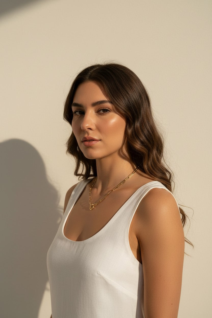 This series of portraits shows a gold paperclip link necklace worn at the collarbone, featuring an elongated oval-link chain that centers on a polished circular ring clasp as a modern, sculptural focal point. Captured from front-facing and side-profile angles against a crisp white tank top, the necklace is shown at true scale, giving shoppers a clear sense of its bold link proportions and how the round clasp element sits as an intentional design detail rather than a hidden closure