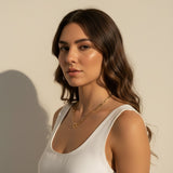 This series of portraits shows a gold paperclip link necklace worn at the collarbone, featuring an elongated oval-link chain that centers on a polished circular ring clasp as a modern, sculptural focal point. Captured from front-facing and side-profile angles against a crisp white tank top, the necklace is shown at true scale, giving shoppers a clear sense of its bold link proportions and how the round clasp element sits as an intentional design detail rather than a hidden closure
