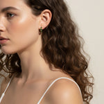 gold baguette hoops on model, huggie hoop earrings worn, emerald huggie hoop earrings, black baguette hoop earrings, clear crystal huggie hoops, gold hoop earrings colorways, baguette stone earrings styled, small gold hoops on ear
