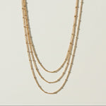 layered satellite necklace flat lay, three strand necklace clasp, cascading gold necklace construction, beaded chain necklace detail, 18k gold satellite chain, graduated necklace flat lay, multi strand necklace clasp detail, delicate layered gold necklace