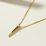 This gold necklace features a sleek dagger-shaped pendant lined with sparkling black pavé crystals, tapering from a wider top edge down to a smooth, polished point for a bold, edgy silhouette. The pendant hangs from a fine box chain, creating a clean, versatile drape that layers effortlessly with other necklaces