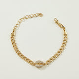 This gold curb chain bracelet pairs a bold, flat-link chain with a pavé crystal cowrie shell charm at the center, creating a coordinated statement piece that matches the cowrie shell choker in the same collection. The chunky curb links offer a substantial, textured base while the crystal-encrusted shell adds sparkle and dimension as the eye-catching focal point. The bracelet fastens with a secure lobster clasp closure and includes a chain extender, allowing for an adjustable, customizable fit around the wri