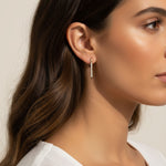 This close-up profile shot shows the longest gold dagger earring worn at the lobe, its tapered pavé crystal spike catching soft light as it extends elegantly downward. Styled with sleek, side-swept waves and a draped white top, the earring is shown at true scale against the jawline, giving shoppers a clear sense of its elongated drop length and sleek, minimal profile. 