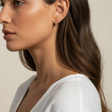 This close-up profile shot shows the longest gold dagger earring worn at the lobe, its tapered pavé crystal spike catching soft light as it extends elegantly downward. Styled with sleek, side-swept waves and a draped white top, the earring is shown at true scale against the jawline, giving shoppers a clear sense of its elongated drop length and sleek, minimal profile.