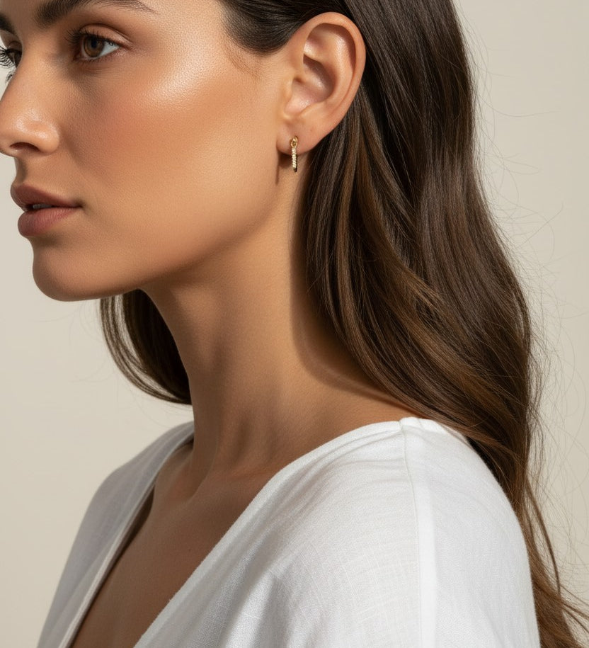 This close-up profile shot shows the longest gold dagger earring worn at the lobe, its tapered pavé crystal spike catching soft light as it extends elegantly downward. Styled with sleek, side-swept waves and a draped white top, the earring is shown at true scale against the jawline, giving shoppers a clear sense of its elongated drop length and sleek, minimal profile.