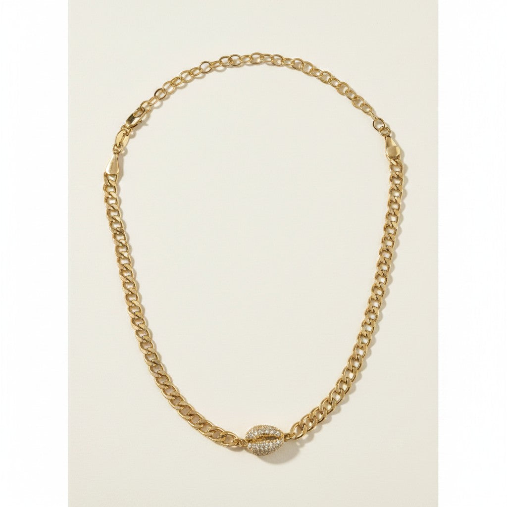 This eye-catching gold choker combines a substantial curb chain link with a delicate cable chain link, creating a striking mix-and-match texture around the neckline. At the center, a cowrie shell charm is fully encrusted in pavé-set crystals, adding sparkle and organic dimension as the statement focal point. The choker fastens with a secure lobster clasp closure, and the interplay between the bold curb links and finer rolo-style links gives the piece a modern, layered look even when worn alone. Photographed