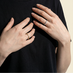 Person wearing a black t-shirt with visible jewelry on a beige background