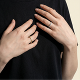 Person wearing a black t-shirt with visible jewelry on a beige background
