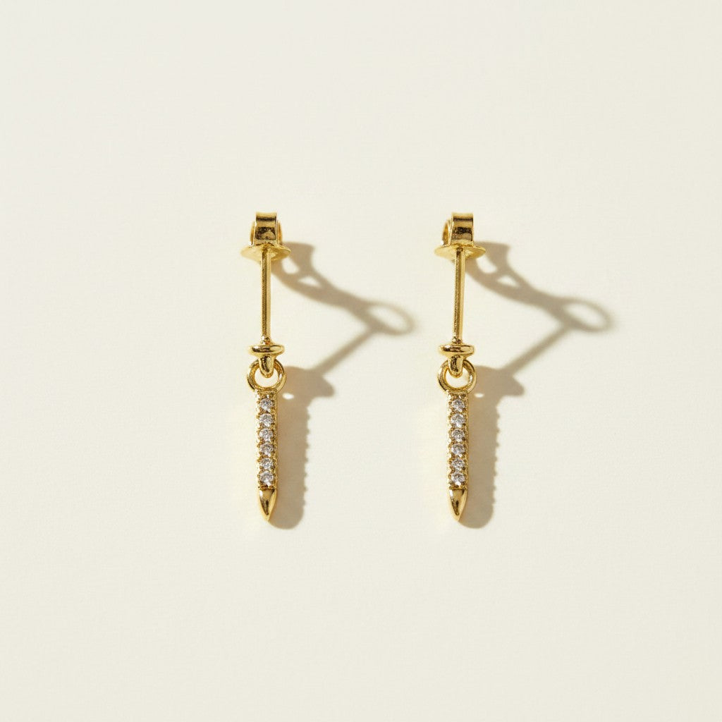 This set showcases a gold dagger-shaped drop earring in three graduated lengths, each featuring a tapered spike lined with sparkling pavé crystals that narrows to a smooth, polished point. The elongated silhouette hangs from a secure post-and-butterfly back closure, offering a sleek, edgy alternative to traditional studs. Photographed flat against a clean, neutral background, the trio displays the earrings' varying drop lengths side by side, highlighting the fine crystal detailing.