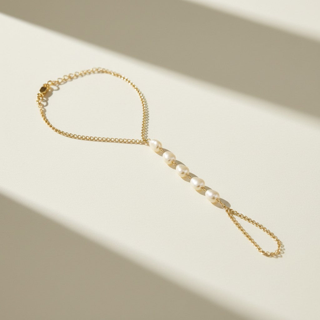 pearl hand chain flat lay, pearl bracelet ring chain, gold hand chain jewelry, pearl slave bracelet detail, hand chain construction, bridal hand jewelry flat lay, delicate pearl hand chain, wrist to finger chain bracelet