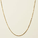 This delicate gold necklace is crafted from a continuous row of tiny flat sequin-like discs linked edge to edge, creating a shimmering, textured chain that catches the light with every angle. The fine, low-profile links lie smooth against the skin, offering a subtle sparkle that pairs beautifully for layering or wearing alone. It fastens securely with a lobster clasp closure and includes a short oval-link extender chain with a polished ball-chain detail, allowing for an adjustable, customizable fit.