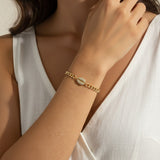 This close-up lifestyle shot shows a gold curb chain bracelet resting elegantly on the wrist, with the pavé crystal cowrie shell charm sitting front and center as the piece's focal point. Styled with a white linen wrap top, the bracelet's bold chain links and sparkling shell charm are shown at true scale against warm skin tones, giving shoppers a clear sense of fit and drape. Soft, warm natural lighting and a relaxed hand-to-collarbone pose lend the image an intimate, editorial feel, highlighting the interp