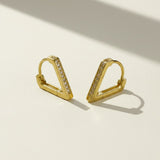 A pair of gold geometric hoop earrings with a row of small clear stones, displayed on a light beige surface with soft shadows.