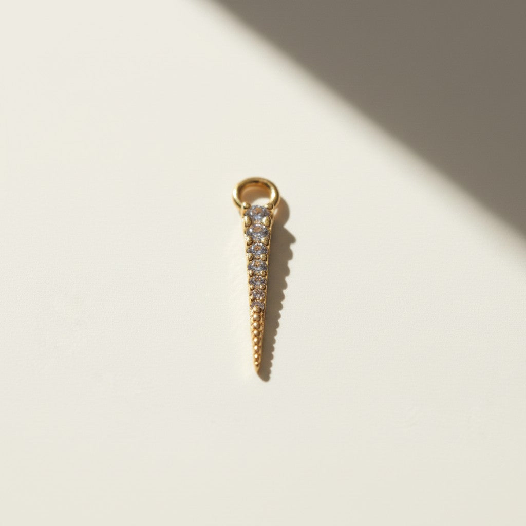 bold CZ spear earring charm — a tapered gold spike lined with a graduated row of sparkling cubic zirconia stones that narrows to a fine, polished point. Crafted in 18k gold overlay, this 20mm charm is designed to attach easily via its jump ring to our 9mm or 11mm seamless hoops (sold separately), letting you customize your hoops with a touch of shimmer and edge.