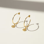 gold coin charm earrings, coin hoop earrings, gold hoop earrings with charm, vintage coin jewelry, dangle hoop earrings flat lay, medallion earrings, engraved coin earrings, everyday gold jewelry
