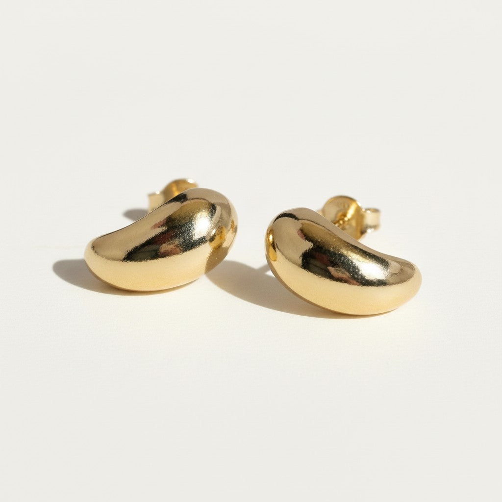 chunky gold dome earrings flat lay, bean shaped gold earrings, sculptural gold stud earrings, high polish gold earrings detail, statement dome earrings, gold earrings push back, modern minimalist gold earrings, glossy gold stud earrings