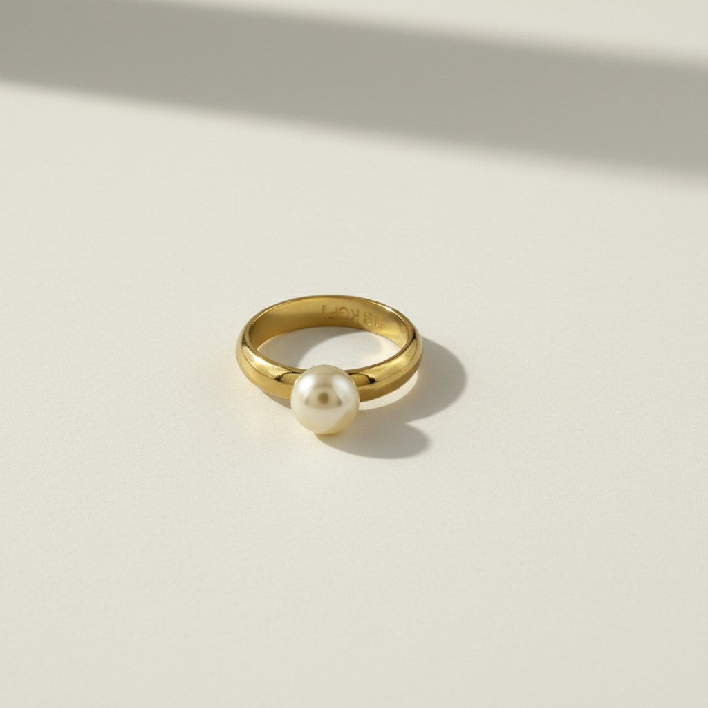 This 18k gold filled ring features a smooth, rounded domed band paired with a single freshwater pearl seated flush against one edge, creating a modern take on a classic solitaire silhouette. The pearl's soft luster contrasts beautifully with the ring's high-polish gold finish, while the substantial, rounded band offers a comfortable, everyday-wearable fit