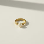 This 18k gold filled ring features a smooth, rounded domed band paired with a single freshwater pearl seated flush against one edge, creating a modern take on a classic solitaire silhouette. The pearl's soft luster contrasts beautifully with the ring's high-polish gold finish, while the substantial, rounded band offers a comfortable, everyday-wearable fit