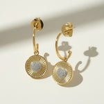 sunburst disc earrings flat lay, gold drop earrings detail, heart pavé earrings pair, huggie hoop drop earrings, textured gold earrings, statement drop earrings, sparkle disc earrings, gold heart earrings