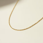 This delicate gold necklace is crafted from a continuous row of tiny flat sequin-like discs linked edge to edge, creating a shimmering, textured chain that catches the light with every angle. The fine, low-profile links lie smooth against the skin, offering a subtle sparkle that pairs beautifully for layering or wearing alone. It fastens securely with a lobster clasp closure and includes a short oval-link extender chain with a polished ball-chain detail, allowing for an adjustable, customizable fit.
