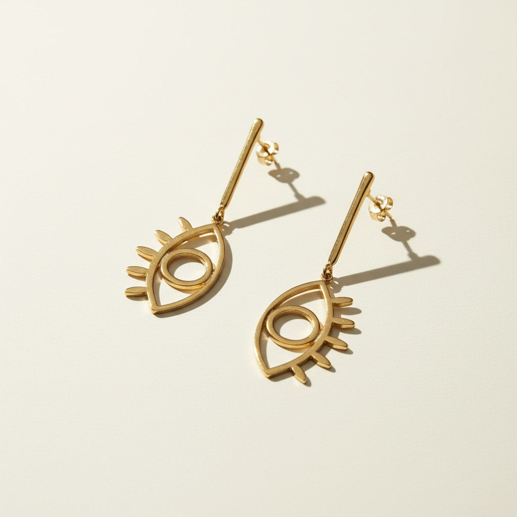 evil eye drop earrings, gold cutout earrings, matte gold dangle earrings, symbolic jewelry, geometric drop earrings, minimalist gold earrings, statement drop earrings flat lay, open linework earrings