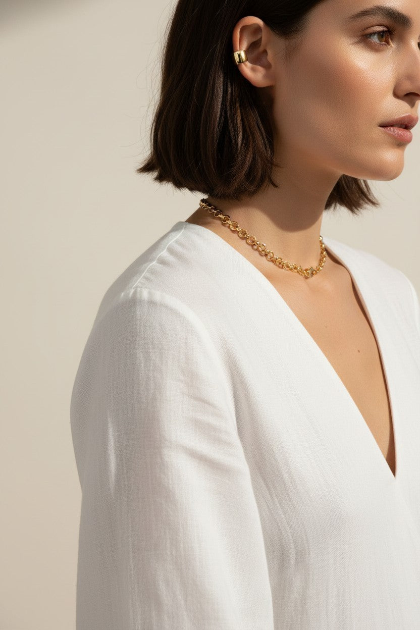 This close-up profile shot captures a chunky gold dome ear cuff wrapped around the upper ear, its smooth, rounded silhouette catching warm natural light for a rich, polished shine. Styled with a sleek dark bob and a draped white top, the cuff sits securely along the ear's outer edge with no piercing required, giving shoppers a clear, true-to-scale view of its bold, wide-band fit. The soft golden-hour lighting and clean profile angle highlight the cuff's smooth curves and glossy gold finish, showing how the 