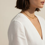 This close-up profile shot captures a chunky gold dome ear cuff wrapped around the upper ear, its smooth, rounded silhouette catching warm natural light for a rich, polished shine. Styled with a sleek dark bob and a draped white top, the cuff sits securely along the ear's outer edge with no piercing required, giving shoppers a clear, true-to-scale view of its bold, wide-band fit. The soft golden-hour lighting and clean profile angle highlight the cuff's smooth curves and glossy gold finish, showing how the 