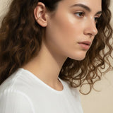 This Gold Beaded Ear Cuff takes a minimalist approach to ear styling with a delicate row of small polished gold beads curving along the upper cartilage. Shown here in close-up profile on a model with soft curls and a relaxed white top, the cuff sits neatly at the top of the ear for a subtle, no-piercing accent that layers beautifully with studs or hoops. Its slim