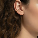 This Gold Beaded Ear Cuff takes a minimalist approach to ear styling with a delicate row of small polished gold beads curving along the upper cartilage. Shown here in close-up profile on a model with soft curls and a relaxed white top, the cuff sits neatly at the top of the ear for a subtle, no-piercing accent that layers beautifully with studs or hoops. Its slim