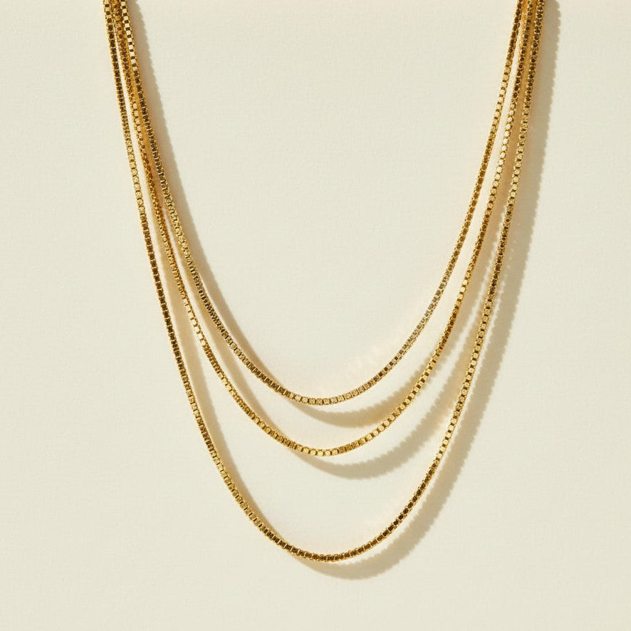 layered box chain necklace flat lay, cascading gold necklace clasp, multi strand necklace detail, box chain construction, 18k gold layered necklace, graduated chain necklace clasp, gold necklace extender chain, delicate box link chain