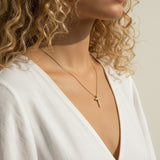 Gold Pavé Cross Pendant Necklace Worn On-Model, This series of portraits shows the gold pavé cross pendant resting at the collarbone on a fine ball chain, styled with a flowing white wrap top for a soft, natural look. Captured from front-facing and close-up profile angles, the crystal-covered cross is shown at true scale against warm skin, giving shoppers a clear sense of its petite, delicate proportions and dainty drop length.