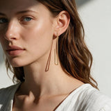 long gold rectangle earrings on model, geometric wire earrings, minimalist gold drop earrings, elongated open hoop earrings, modern gold earrings, lightweight statement earrings, architectural earrings, thin gold wire earrings, contemporary gold jewelry, linear gold earrings, women’s geometric earrings, elegant everyday earrings