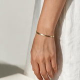 gold herringbone bracelet on wrist, flat gold chain bracelet, slim snake chain bracelet, dainty gold bracelet, minimalist gold bracelet, adjustable gold bracelet, everyday gold bracelet, layering bracelet, shiny gold chain bracelet, women’s gold bracelet, flat herringbone bracelet, sleek wrist jewelry