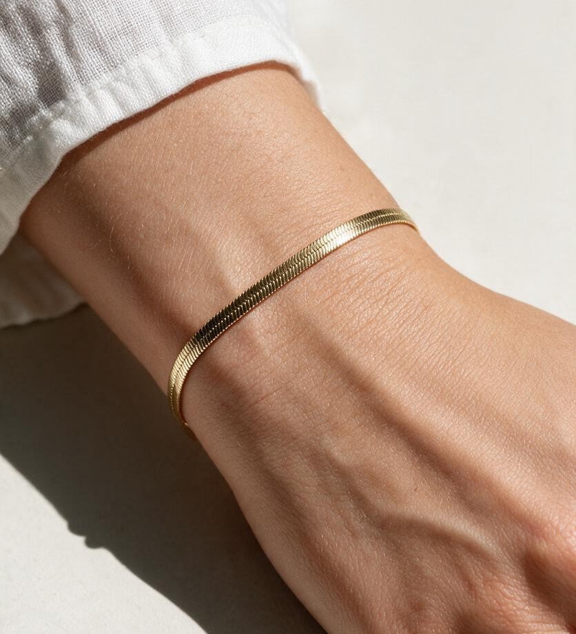 gold herringbone bracelet on wrist, flat gold chain bracelet, slim snake chain bracelet, dainty gold bracelet, minimalist gold bracelet, adjustable gold bracelet, everyday gold bracelet, layering bracelet, shiny gold chain bracelet, women’s gold bracelet, flat herringbone bracelet, sleek wrist jewelry